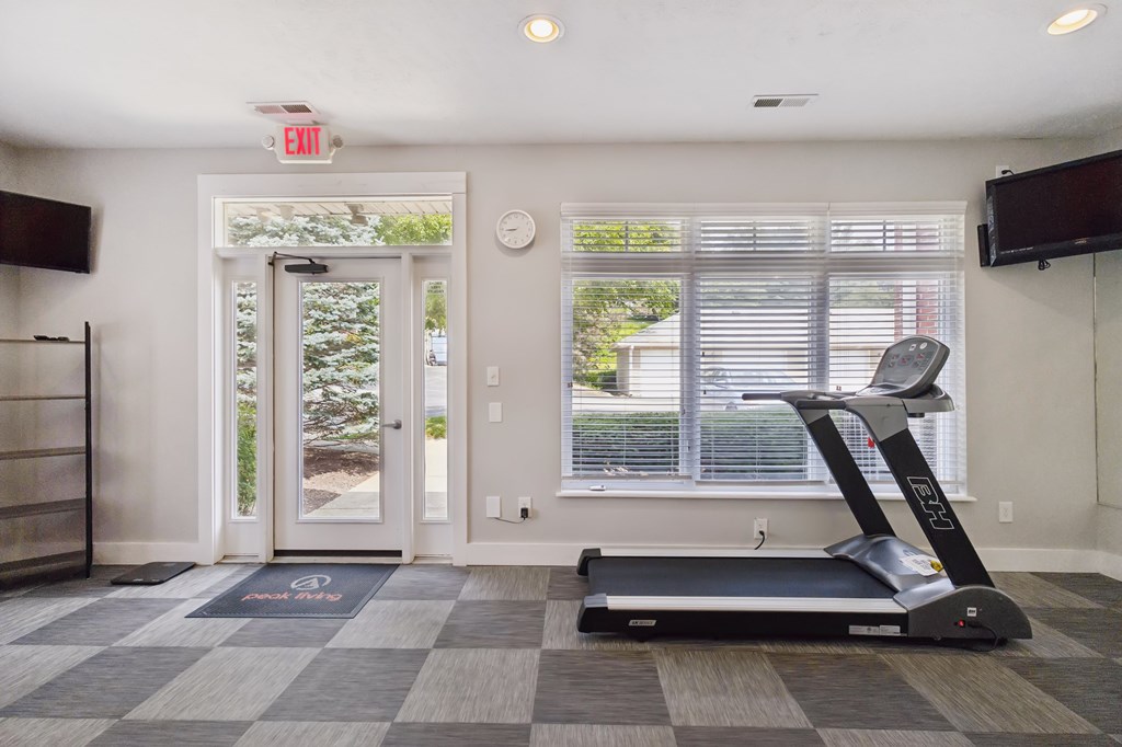 A treadmill is in a room with a window and a clock on the wall.