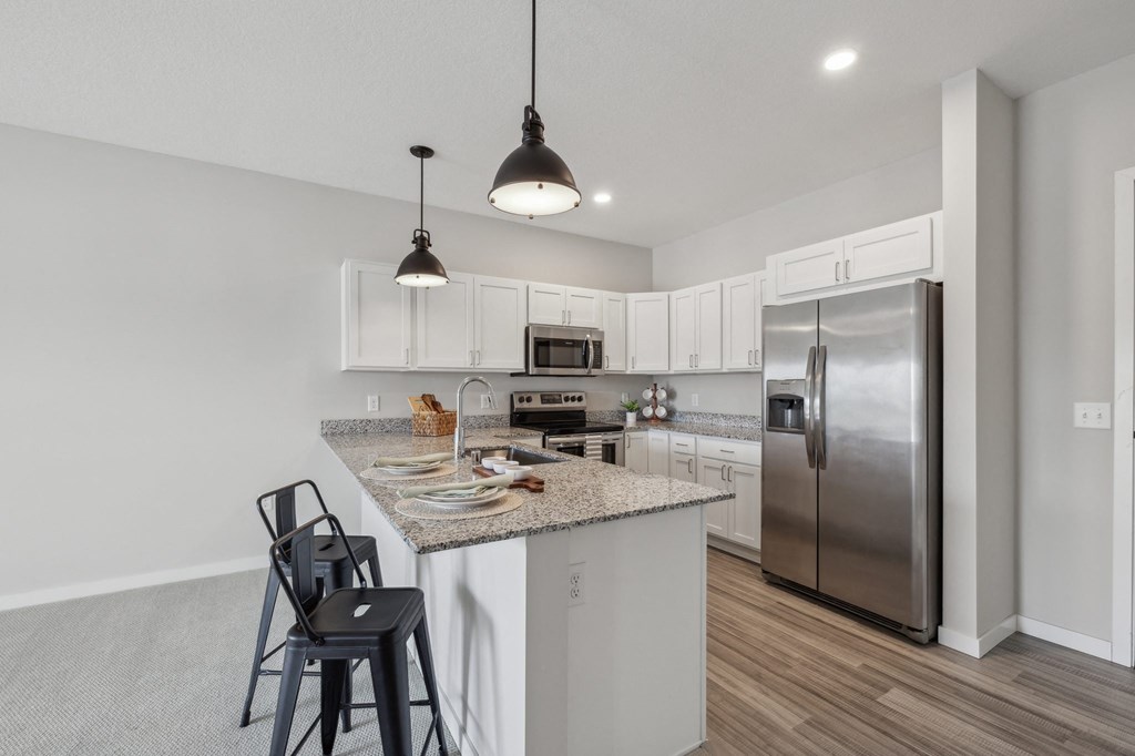 a kitchen with a island with bar stools and a stainless steel refrigerator at The Hendrickson, Falcon Heights, Minnesota