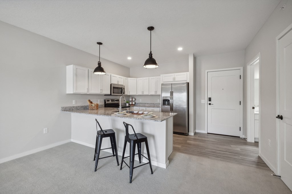 an open kitchen and dining area with bar stools in a new home at The Hendrickson, Falcon Heights, Minnesota