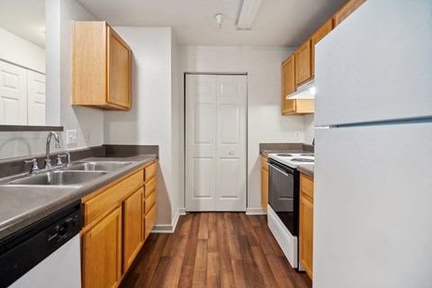 a kitchen with white appliances and wood flooring and a door to a hallway