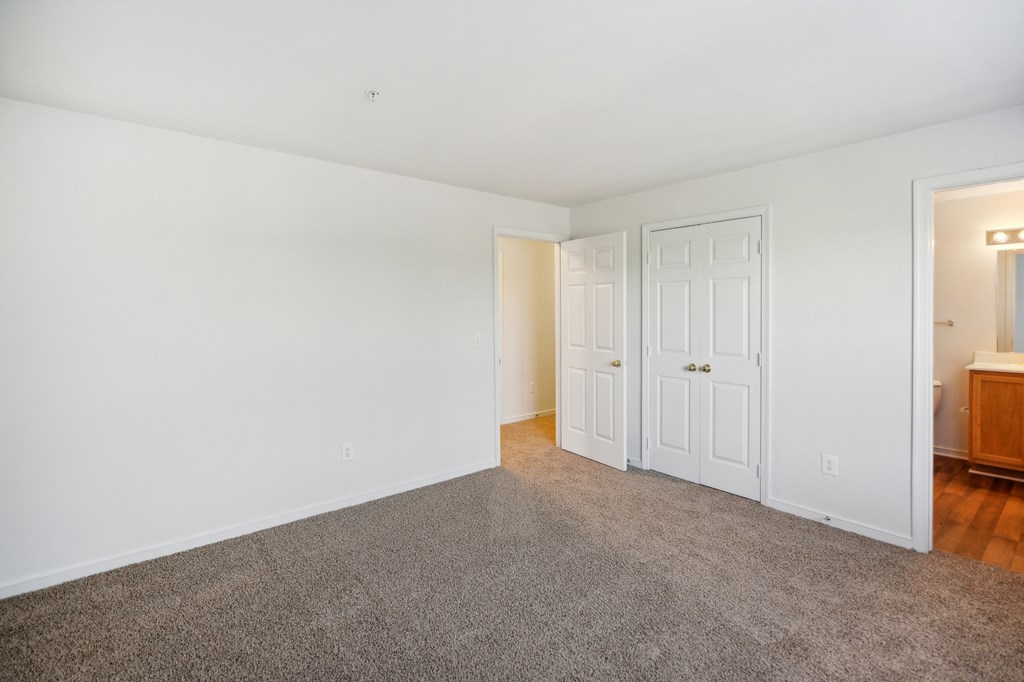 a bedroom with white walls and carpet and a door to a bathroom