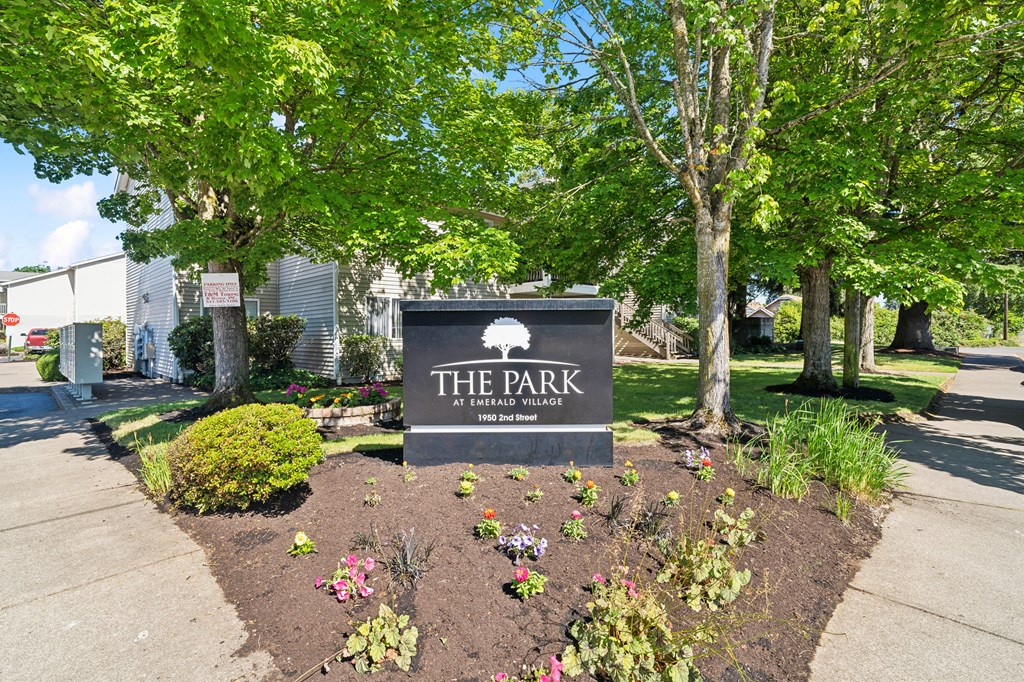 a park with a sign and trees and flowers