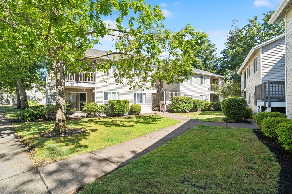 a walkway between two white houses with trees and grass