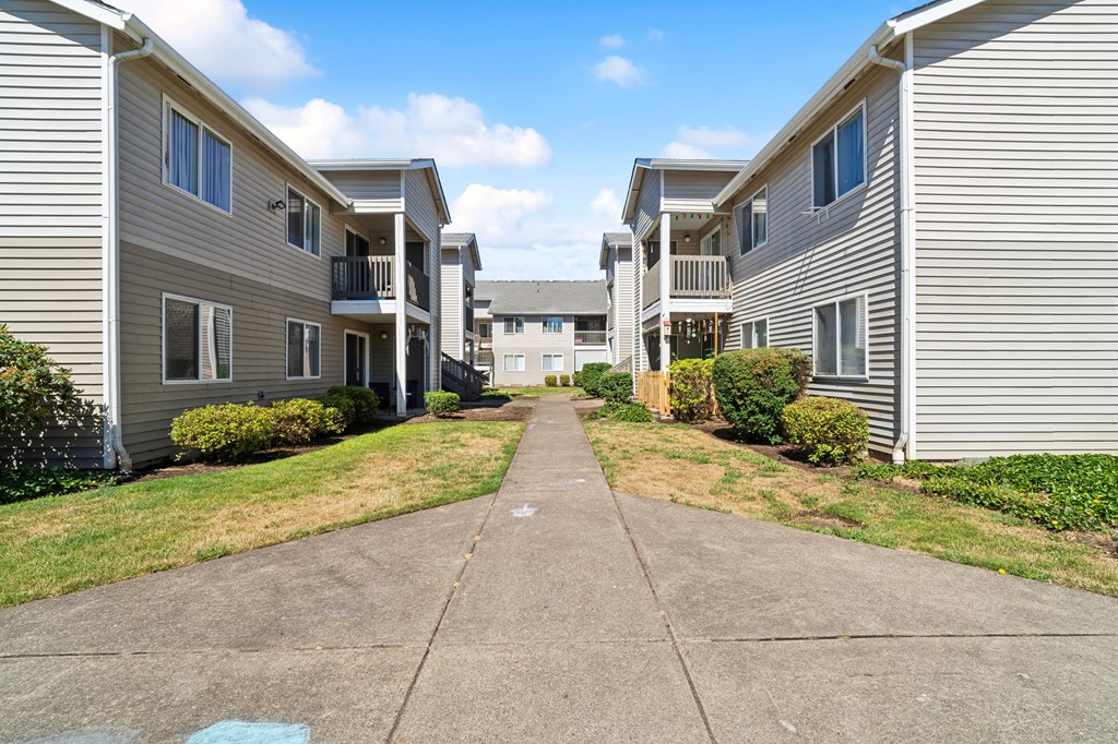 a pathway between two apartment buildings with grass and bushes