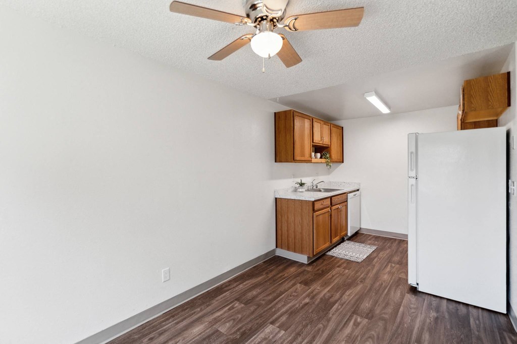 an empty kitchen with a refrigerator and a ceiling fan