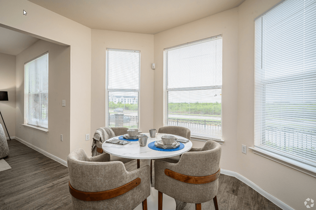 a dining area with a table and chairs and three large windows