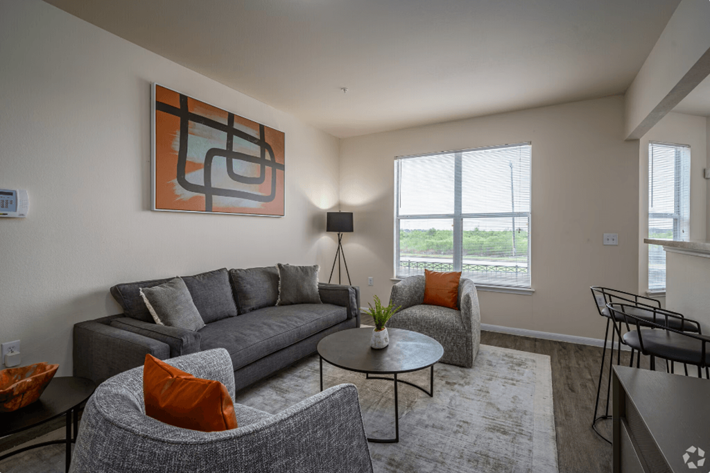 a living room with grey couches and orange pillows