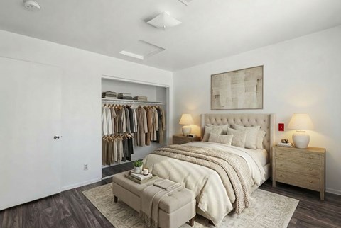 A bedroom with a large bed, a clothing rack, and a nightstand with lamps.