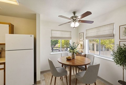 A dining room with a white refrigerator and a round wooden table with four grey chairs.