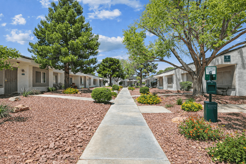 A concrete pathway leads through a row of houses with trees on either side.