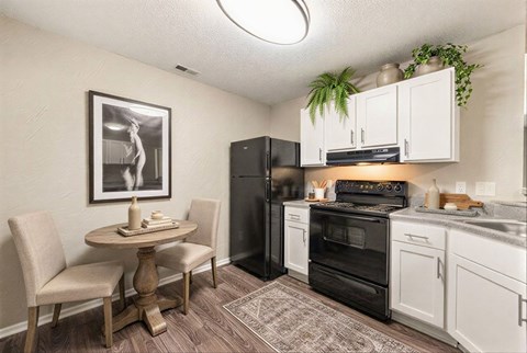 A kitchen with a black refrigerator, white cabinets, and a table with chairs.