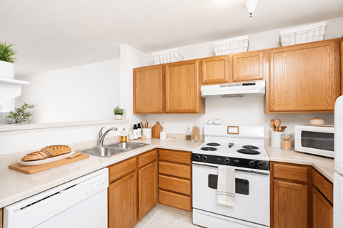 A kitchen with a white stove top oven and wooden cabinets.