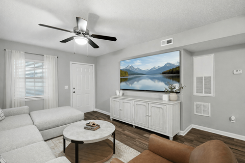 A living room with a white couch, a coffee table, and a television displaying a mountain landscape.