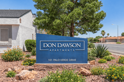 A blue sign that says "Don Dawson Apartments" in front of a building.