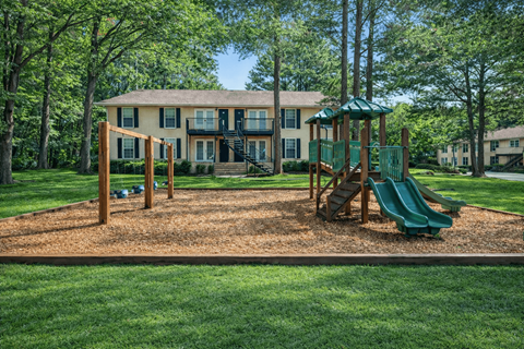 A playground with a green slide and a wooden swing set in front of a two-story house.