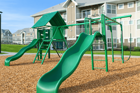 A green playground slide in front of apartment buildings.
