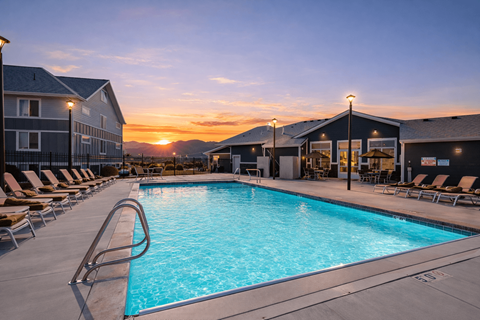 A sunset view of a pool area with lounge chairs and a building in the background.