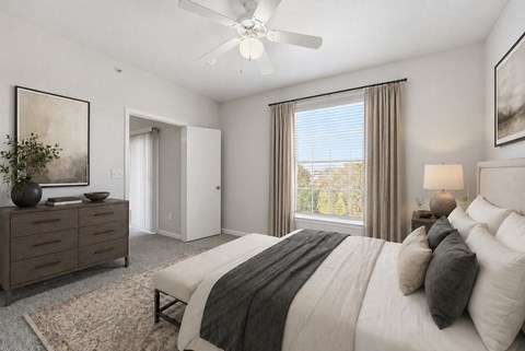 A bedroom with a large bed, a ceiling fan, and a dresser with a vase on top.