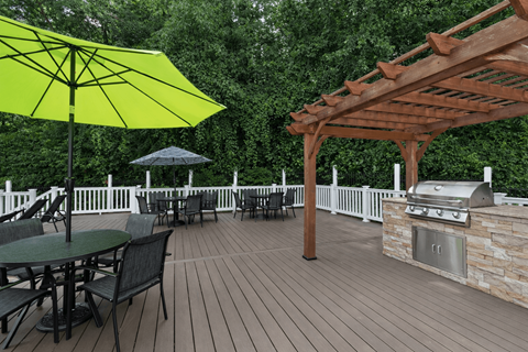 A yellow umbrella is on a wooden deck with a grill and chairs.