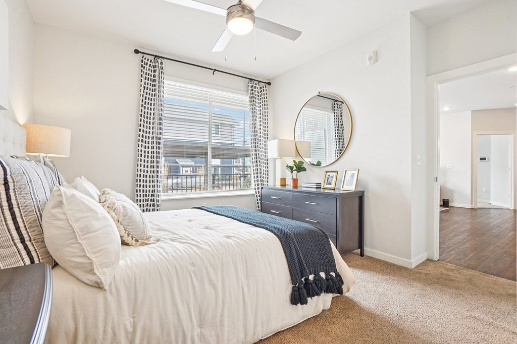 A bedroom with a bed, nightstand, and a window with a view of a balcony. at Connect at First Creek Apartments, Denver, CO