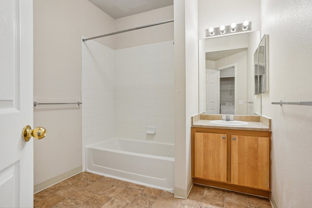 A white bathroom with a wooden cabinet and a white tub. at Stetson Meadows Apartments, Colorado