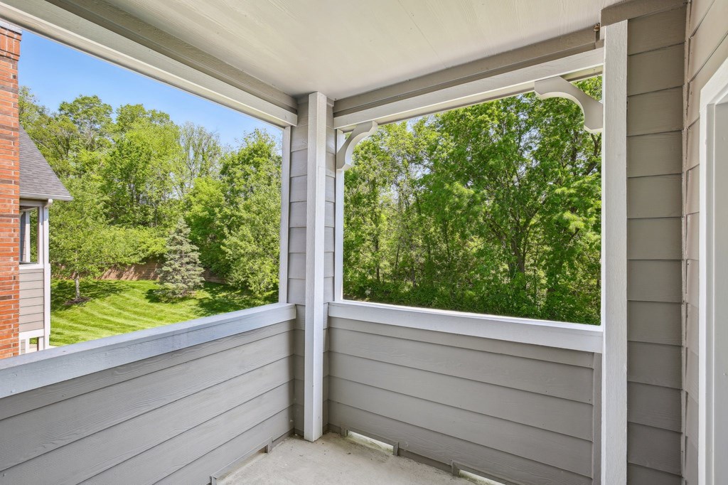 A sunny day with a view of a green lawn and trees from a covered porch. at Province of Briarcliff Apartments, Kansas City