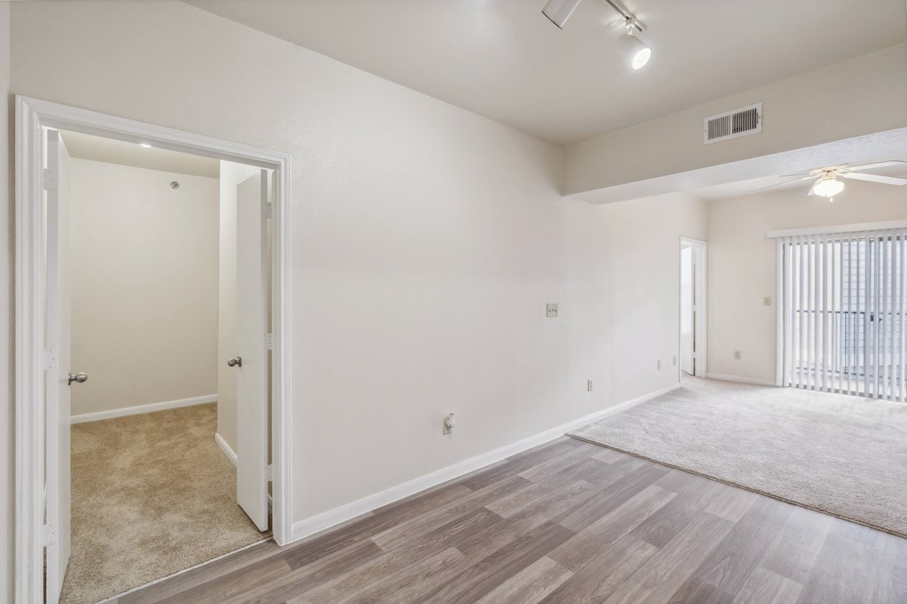 the living room and dining room of an apartment with white walls and wood flooring