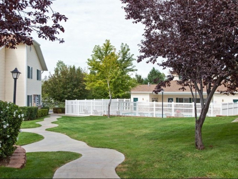 a sidewalk through a yard in front of a house with a white fence