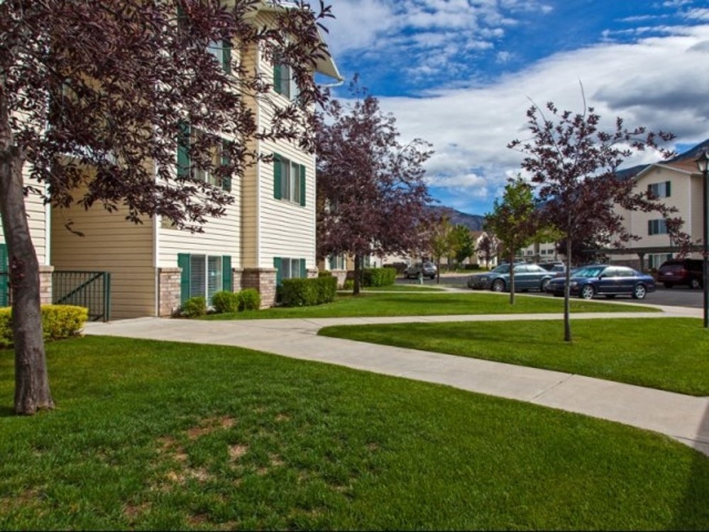 a sidewalk in front of a building with grass and trees