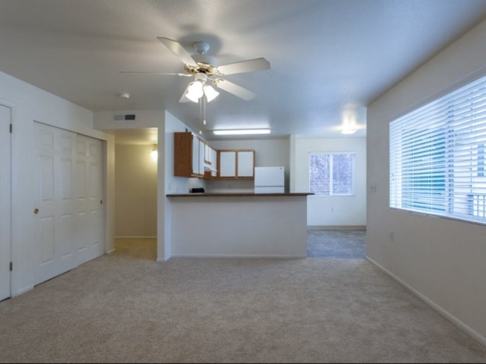 an empty living room with a ceiling fan and a kitchen