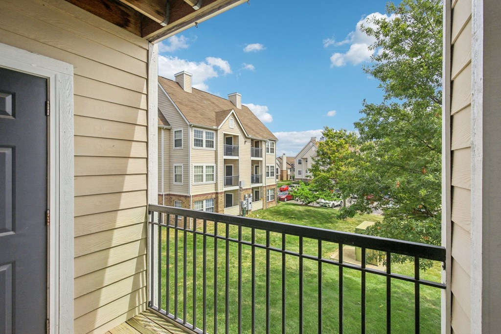A balcony with a black railing overlooks a grassy area and apartment buildings.
