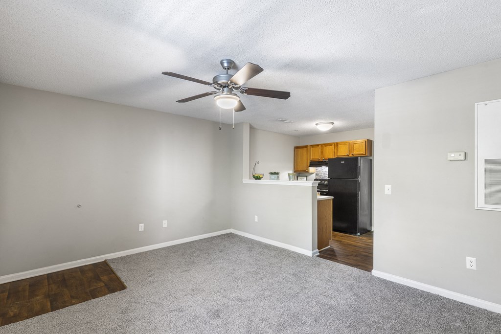 an empty living room with a ceiling fan and a kitchen