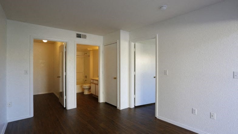 an empty living room with a wooden floor and a toilet