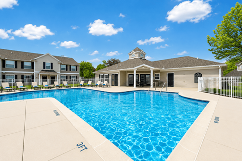 A large swimming pool in front of a building with a white fence around it.