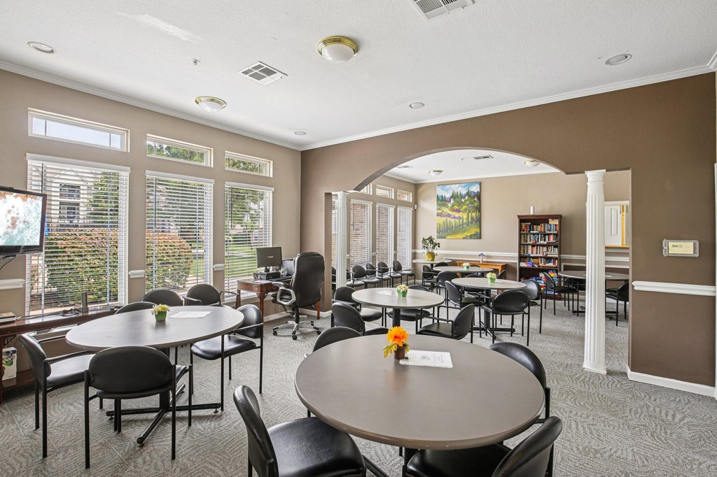 A room with tables and chairs and a vase of flowers on the table.