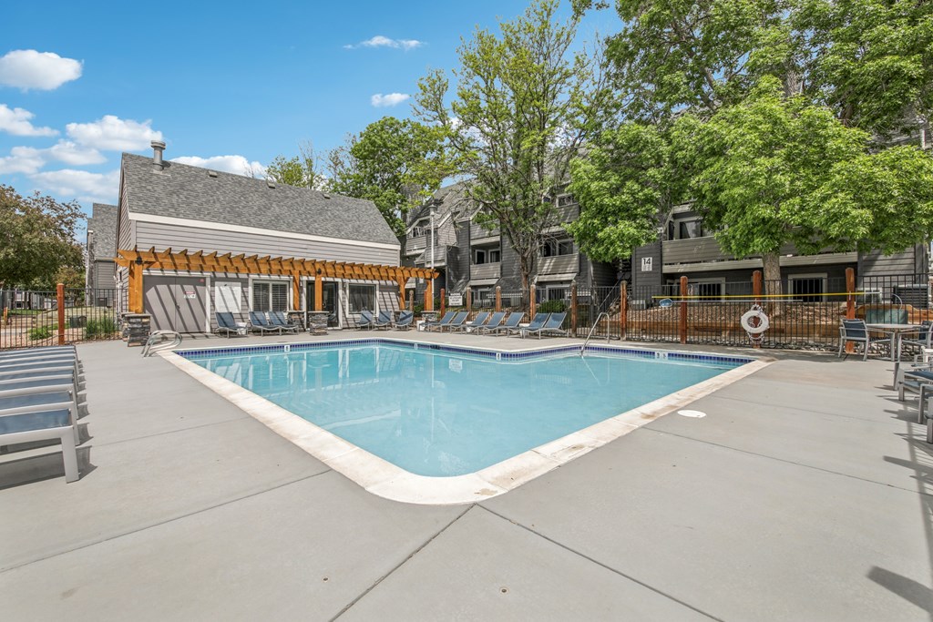 A large outdoor swimming pool surrounded by a concrete patio and lounge chairs.