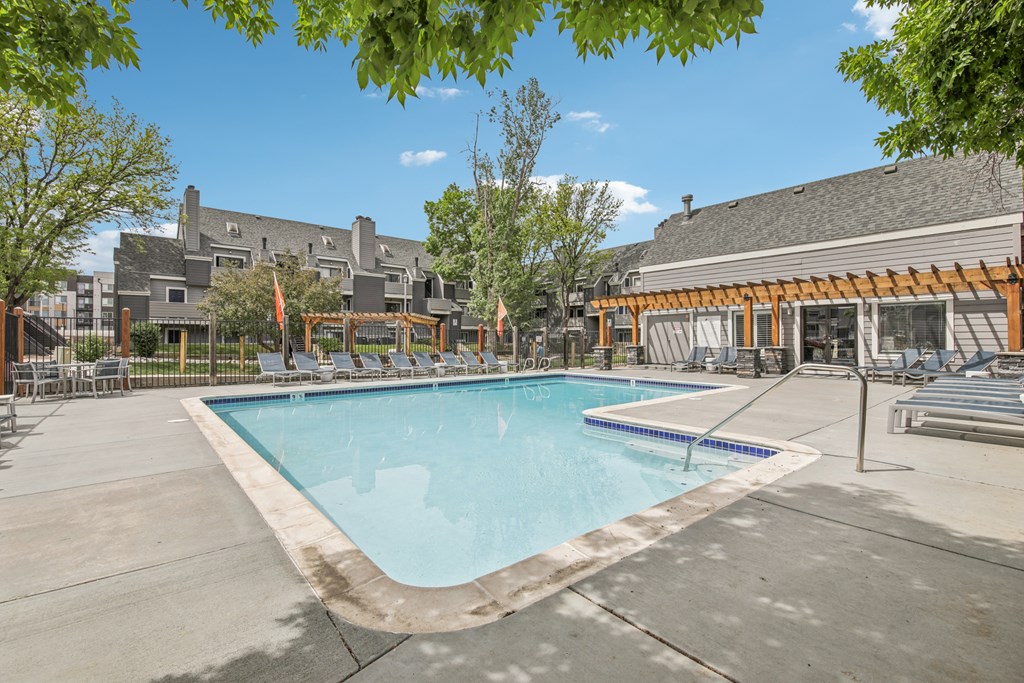 A large swimming pool surrounded by a concrete patio and a wooden pergola.