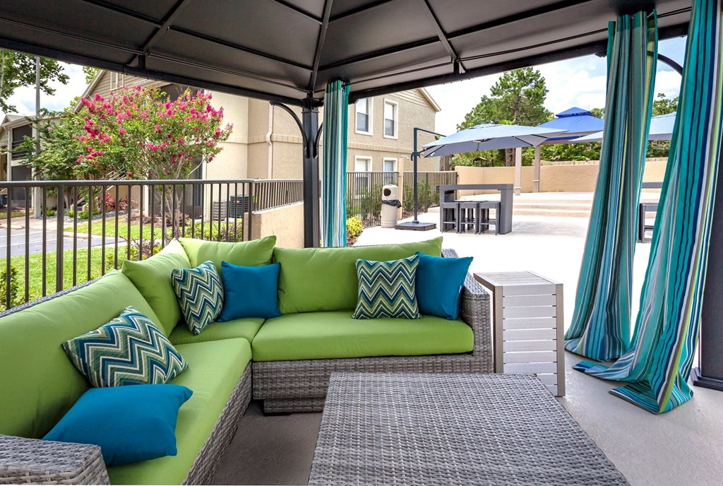 a covered patio with green couches and blue and green pillows