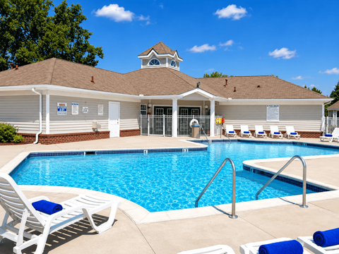 A pool area with a building and lounge chairs.