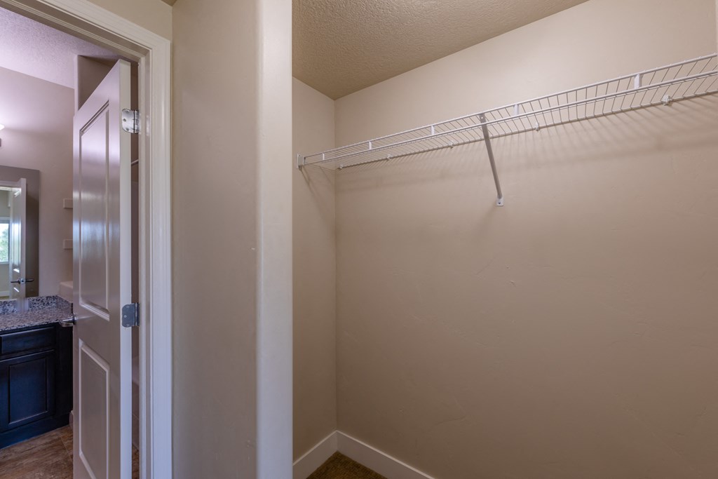 A walk in closet with a white door and a white shelf.