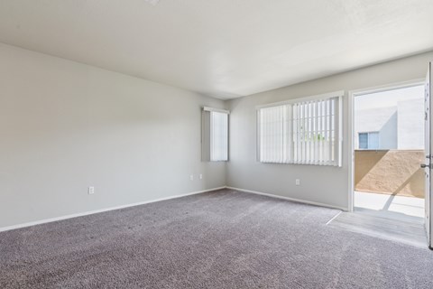 the living room of an apartment with carpet and a door to the patio