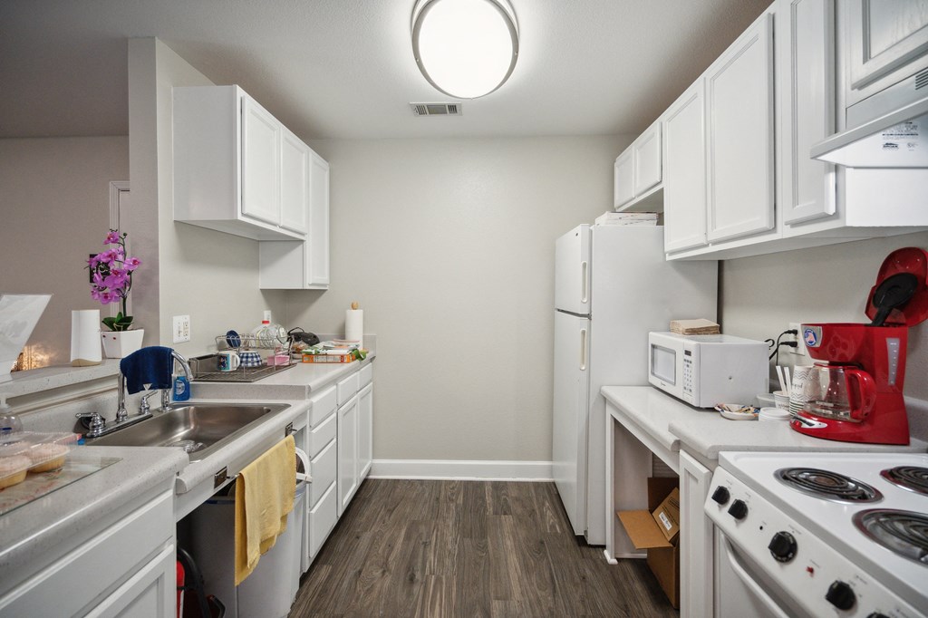 A kitchen with white cabinets and a red kettle on the stove.