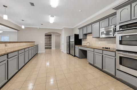 A spacious kitchen with grey cabinets and black appliances.