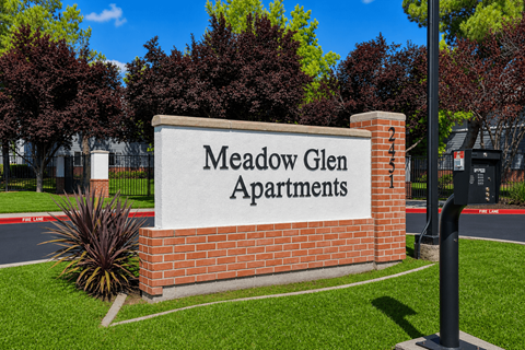 A sign that says Meadow Glen Apartments in front of a building.