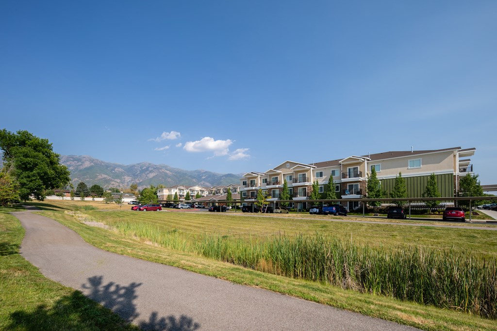 A road with grass on the side and apartment buildings in the background.