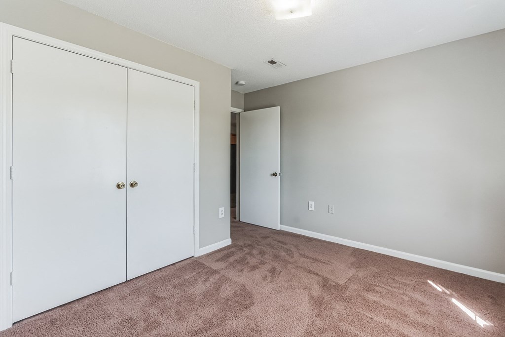an empty bedroom with white closets and carpeting