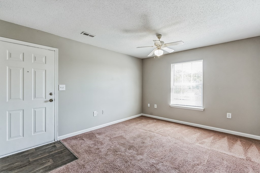an empty living room with a white door and a ceiling fan