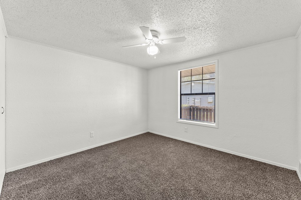 an empty living room with a ceiling fan and a window