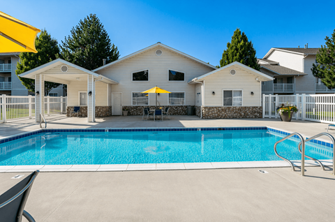A swimming pool in front of a house with a yellow umbrella.