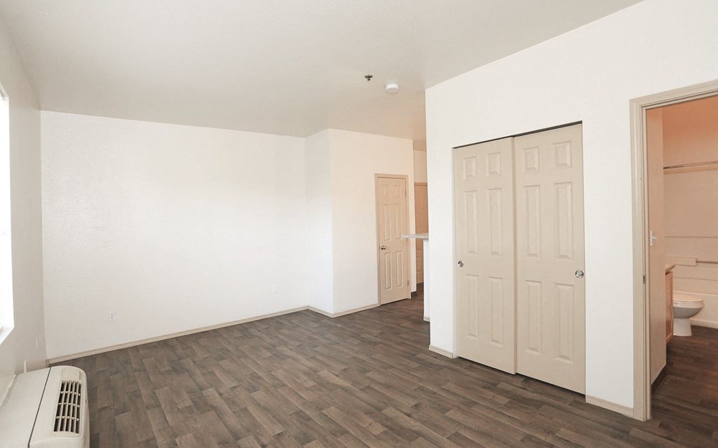an empty living room with white walls and wood flooring and a door to a